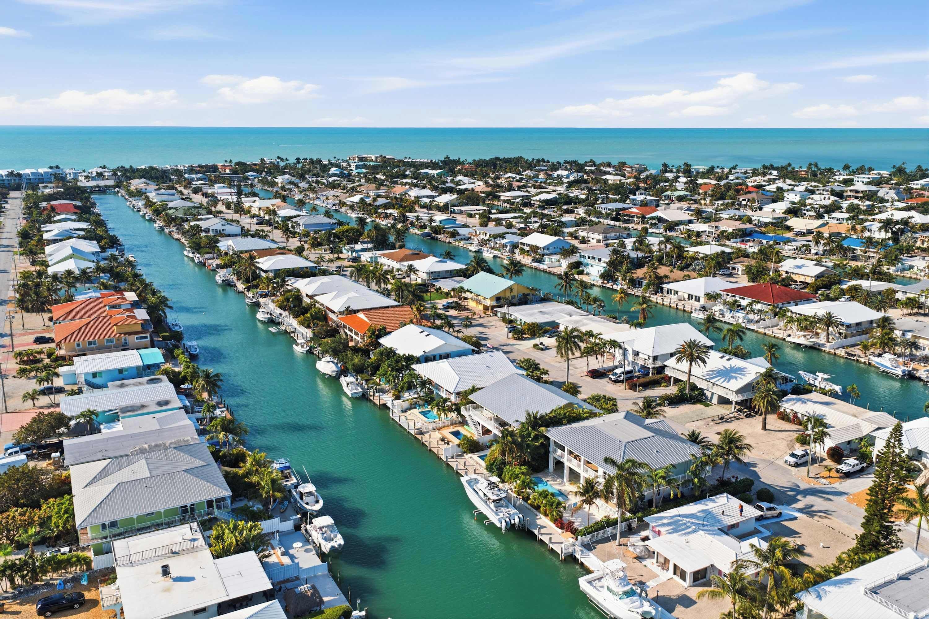 Un quartier résidentiel situé sur la côte, avec des maisons construites le long d’un canal, dont certaines sont dotées de balcons apparents et bordant une marina.