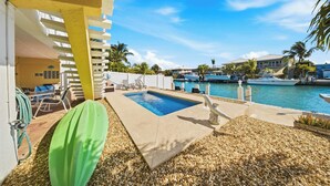 A pool area with a clear blue pool, a green lounge chair, and a view of the marina with boats. - Sea Dreams on 9, 3 bedroom 3 bath 1/2 duplex, Private Pool in Key Colony Beach waterfront with 37 ft dockage and cabana club private membership, pool table and putting green. (Key Colony Beach)