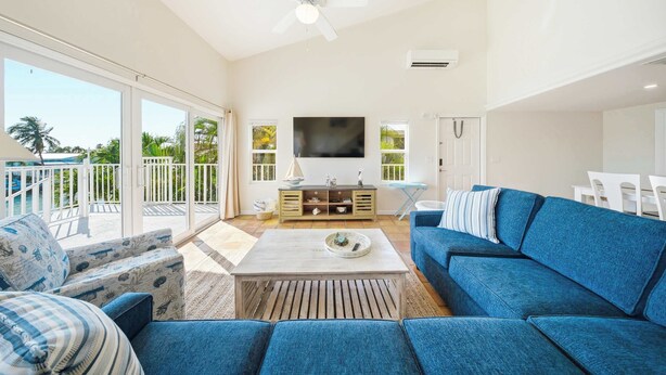 A spacious living area with a large sofa, a coffee table, and a TV mounted on the wall. - Sea Dreams on 9, 3 bedroom 3 bath 1/2 duplex, Private Pool in Key Colony Beach waterfront with 37 ft dockage and cabana club private membership, pool table and putting green. (Key Colony Beach)