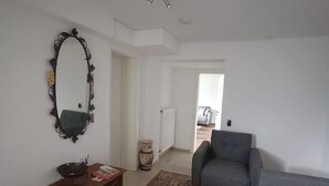Un salón con un sofá gris, un tapete estampado, una mesita de madera con un cuenco y un libro, un espejo decorativo y un jarrón.