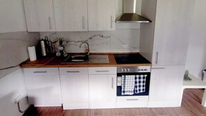 A compact kitchen with white cabinets, a stainless steel sink, a built-in oven, and a black stovetop. - Modern 3-room apartment near Frankfurt (Niddatal)
