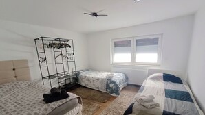 A bedroom with two beds, a ceiling fan, a window with blinds, and a radiator. - Modern 3-room apartment near Frankfurt (Niddatal)