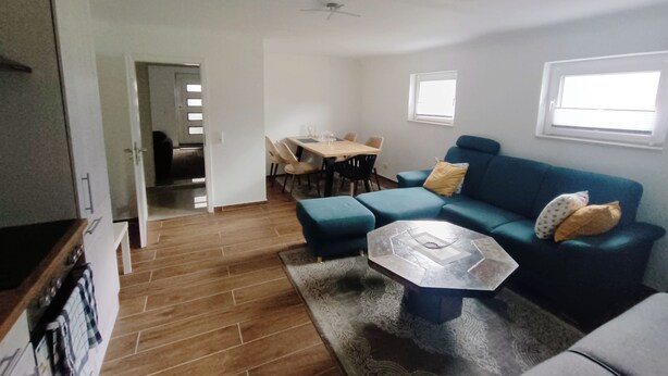 A living room with a blue sofa, a coffee table, and a dining area with chairs. - Modern 3-room apartment near Frankfurt (Niddatal)
