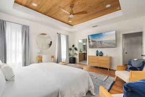 Ein Schlafzimmer mit einem großen Bett, Holzboden, einem Fernseher, einem Schminktisch und einem Spiegel.