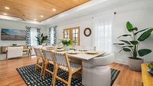 Un comedor con techo de madera, un ventanal con cortinas y una mesa de comedor con sillas.