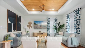 Una sala de estar moderna con ventilador de techo, un cuadro grande, un televisor y un comedor con mesa y sillas.