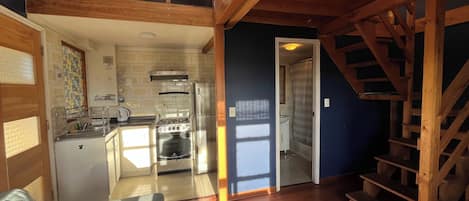Cocina compacta con estufa, refrigerador y comedor con mesa y sillas.