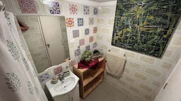 A bathroom with a white sink, a mirror, a wooden shelf with a plant, and a tiled wall with various patterns.
