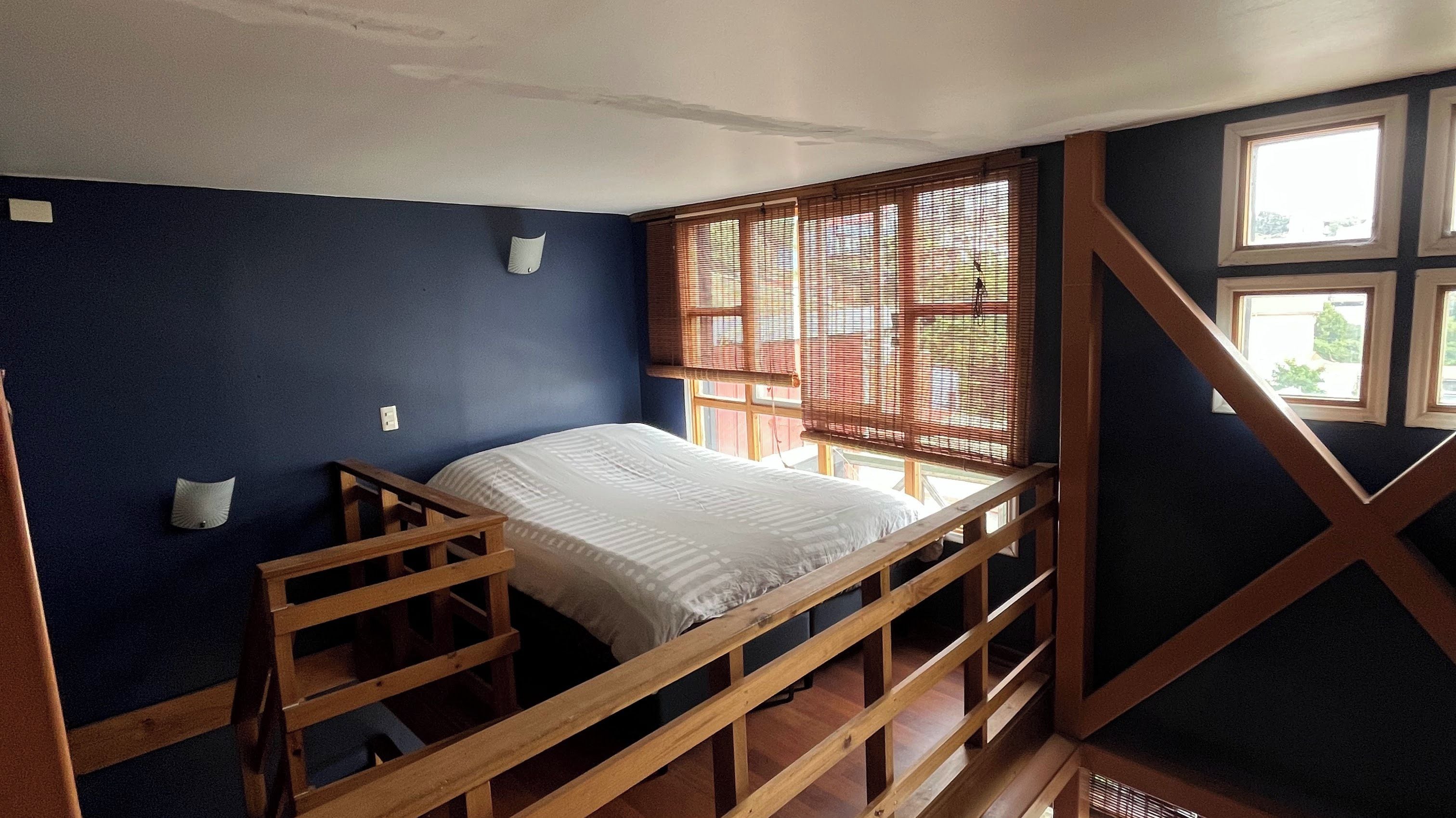A bunk bed in a room with dark walls, a window with blinds, and a wooden railing.