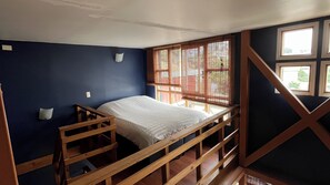 Un lit superposé dans une pièce aux murs sombres, avec une fenêtre munie de stores et une rambarde en bois.