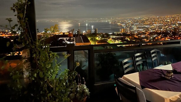 Un balcón con vista a un paisaje urbano nocturno, que incluye una masa de agua y edificios.