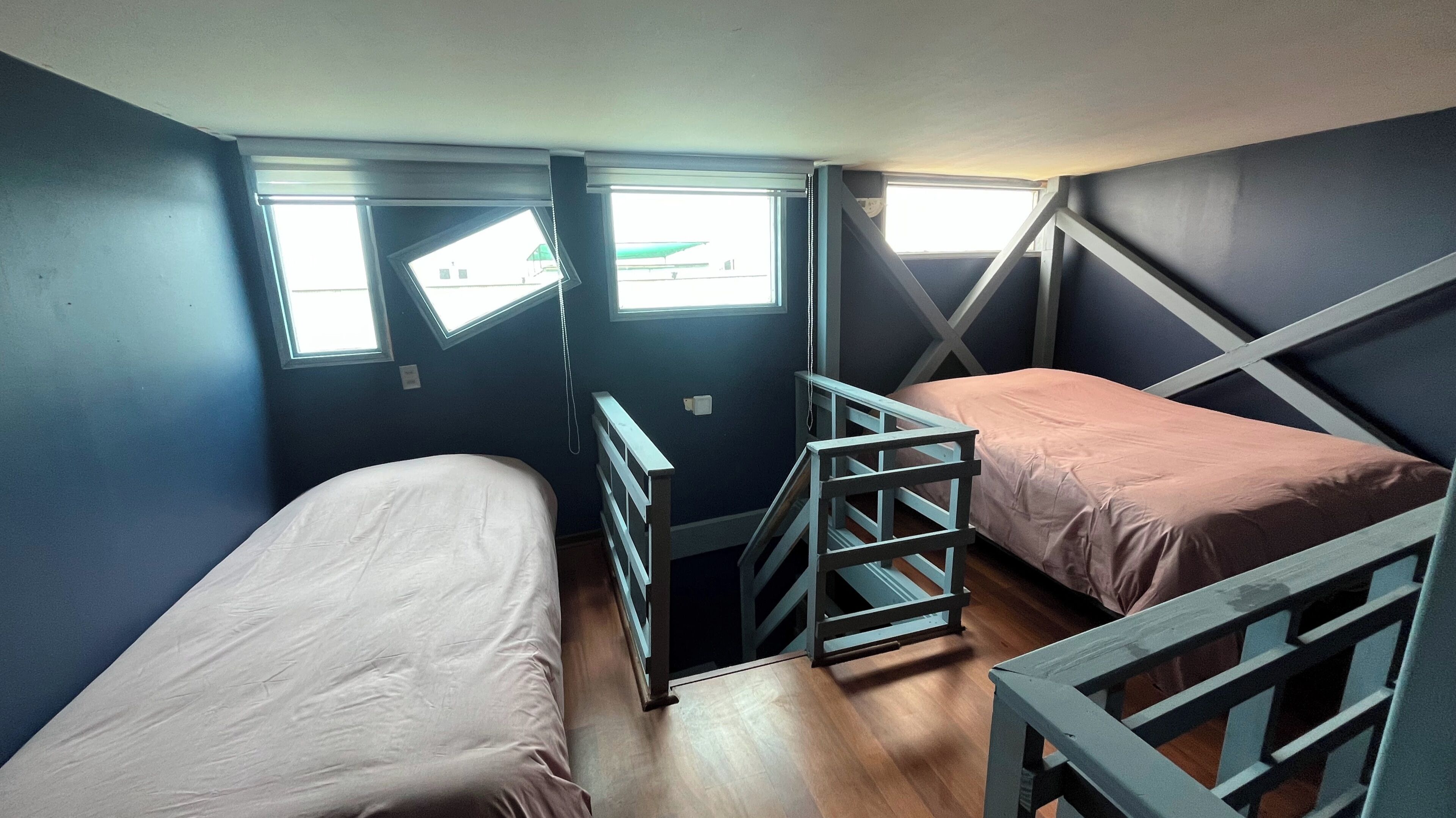 A dormitory room with two bunk beds, a wooden ladder, and a window providing natural light.
