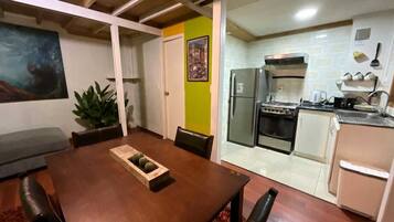 Un comedor con mesa y sillas de madera, una cocina equipada y una pared verde decorativa.