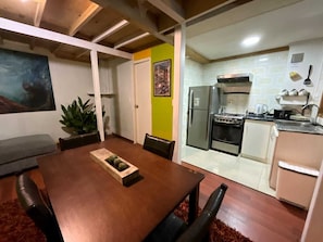 A dining area with a wooden table and chairs, a kitchen with appliances, and a green accent wall. - Apart hotel JaguiHaus (Valparaíso)