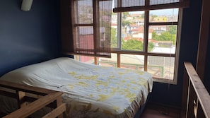 A room with a bed, a window with blinds, and a view of buildings outside. - Apart hotel JaguiHaus (Valparaíso)