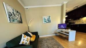 Sala de estar com sofá verde, televisão de tela plana, mesa de centro e tapete estampado.
