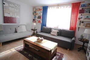 Un salon avec un canapé, une table basse, une bibliothèque et une fenêtre avec des rideaux.