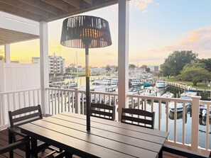 A wooden deck with a table and chairs, overlooking a marina with boats docked. - Waterfront • Heated Decks • Workspace • EV Charging • Home Gym • Downtown (Cambridge)