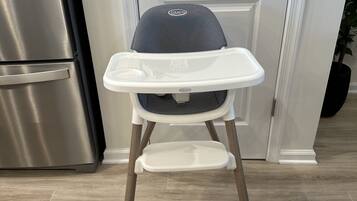 En barnstol med ett brickbord, placerad i ett kök med ett kylskåp i rostfritt stål och en vit dörr.
