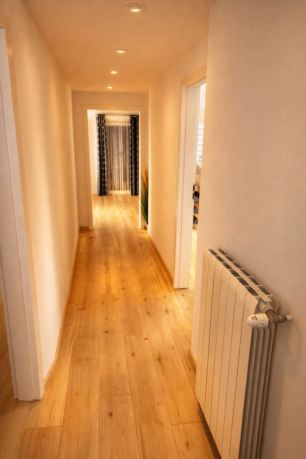 A hallway with wooden flooring, a radiator, and a door leading to a room.