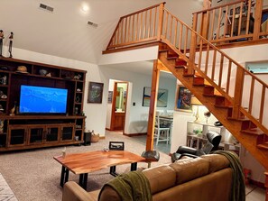 Amplia sala de estar con una escalera de madera, televisor y un rincón de descanso acogedor.