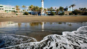 Ein Strand mit einem Leuchtturm, Palmen und einem Gebäude mit blauem Dach.
