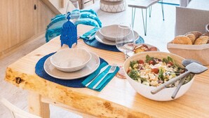 Ein Essbereich mit einem Holztisch, gedeckt für zwei Personen, einer Salat-Schüssel und Blick ins Freie.