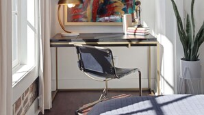 A modern bedroom with a desk, a chair, a bed, a large abstract painting, a lamp, and a potted plant. - Spacious 4BR Condo | Heart of Downtown Savannah (Savannah)
