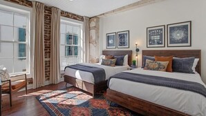 A bedroom with two beds, a patterned rug, a brick wall, and framed pictures on the wall. - Spacious 4BR Condo | Heart of Downtown Savannah (Savannah)