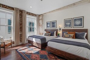 Ein Schlafzimmer mit zwei Betten, einem gemusterten Teppich, einer Ziegelwand und gerahmten Bildern an der Wand.