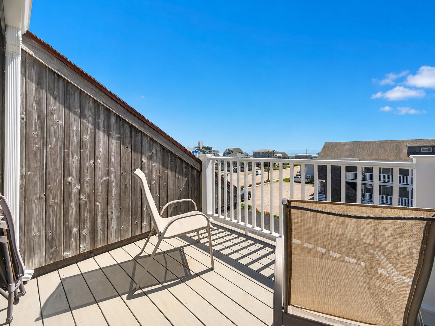 A balcony with a wooden fence, a white chair, and a view of a residential area.