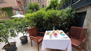 A table set with breakfast items, two wooden chairs, potted plants, and a white umbrella.