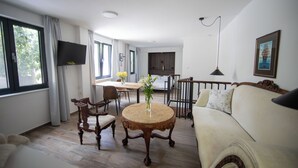A living room with a round wooden table, a sofa, a TV mounted on the wall, and a dining area with chairs and a table.