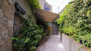 A narrow alleyway with stone walls, potted plants, and a wooden pergola.