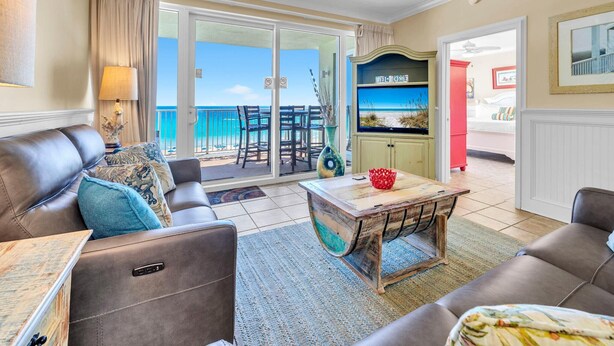 A living room with a sofa, a coffee table, and a TV. There is a balcony with a view of the ocean. - Emerald Isle 508 (Panama City Beach)