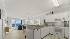 A modern kitchen with white cabinetry, a built-in microwave, and a large island with a sink. - Emerald Isle 508 (Panama City Beach)