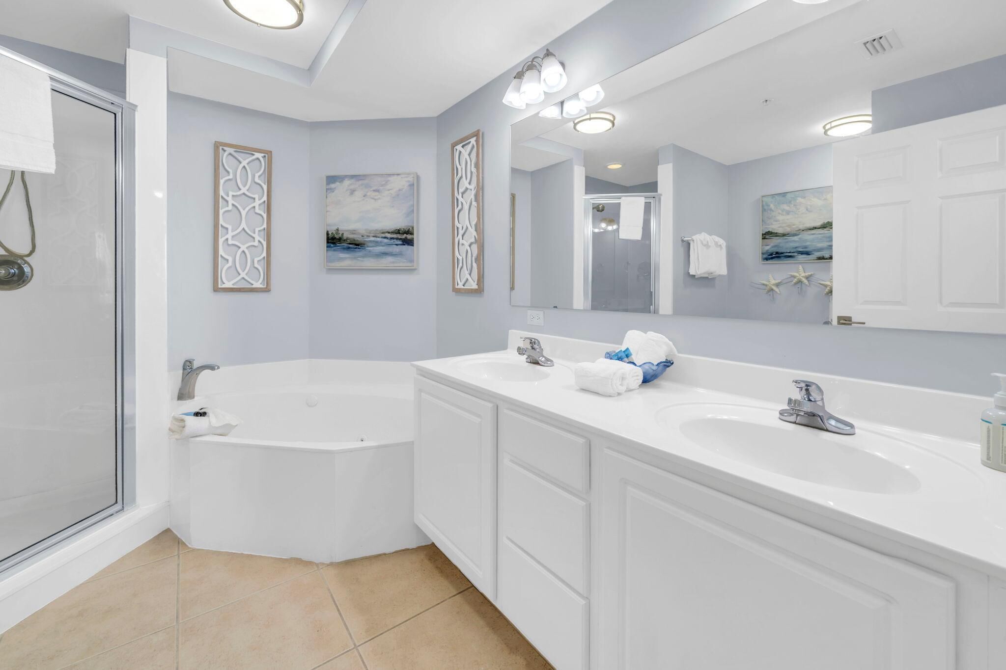Une salle de bain moderne avec une baignoire, deux lavabos, un grand miroir et des œuvres d’art décoratives au mur.