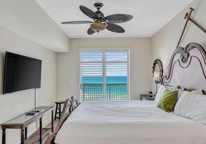 A hotel room with a bed, a ceiling fan, a TV, a small table, and a balcony with a view of the ocean. - Sunrise Beach #1010 (Panama City Beach)