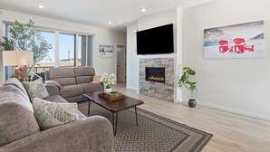 A modern living room with a fireplace, a flat-screen TV, and a large window. - Modern Hideaway with Private Terrace in Downtown (Anchorage)