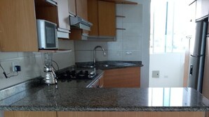Een keuken met een granieten aanrecht, roestvrijstalen apparatuur en drie barkrukken.