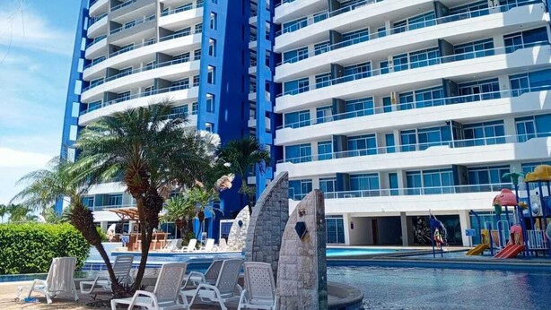 Een hoog hotel met meerdere balkons, een zwembad en palmbomen.