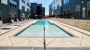 Une piscine dotée de chaises longues et entourée d’une clôture, le tout bordé d’immeubles modernes.
