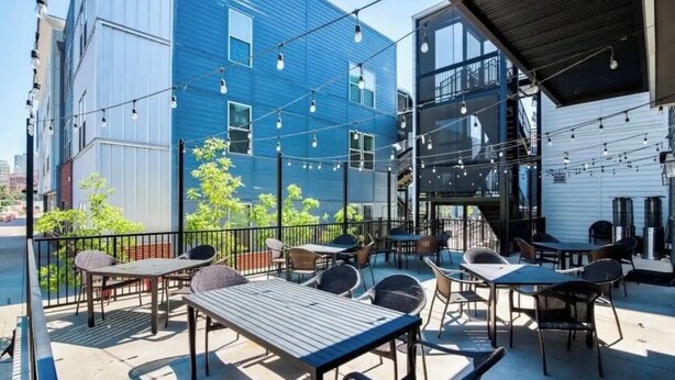 Une terrasse extérieure avec des tables et des chaises, un bâtiment bleu en arrière-plan et des guirlandes lumineuses.
