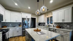 Une cuisine moderne avec des meubles blancs, un îlot central et des luminaires suspendus.