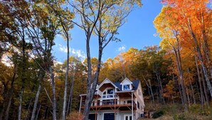 Un chalet à deux étages doté d’un balcon, entouré d’un feuillage automnal.
