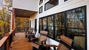 Une terrasse extérieure couverte, dotée de bancs et de tables en bois, de grandes fenêtres et d’un luminaire suspendu.