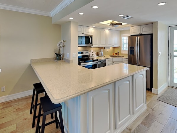 A kitchen with a large island, white cabinetry, stainless steel appliances, and a ceiling fan. - Pointe South 201 (Fort Myers Beach)