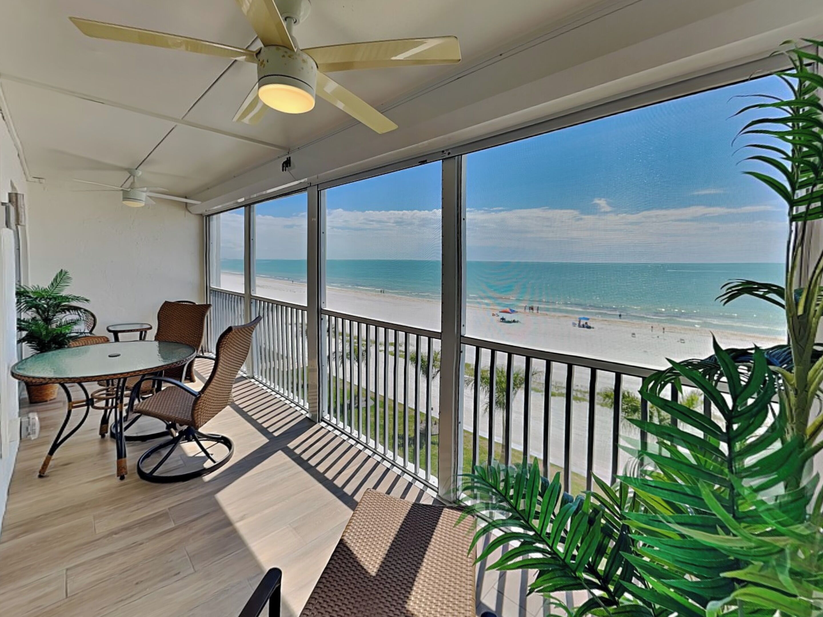 A balcony with a view of the beach, a ceiling fan, and a table with chairs.