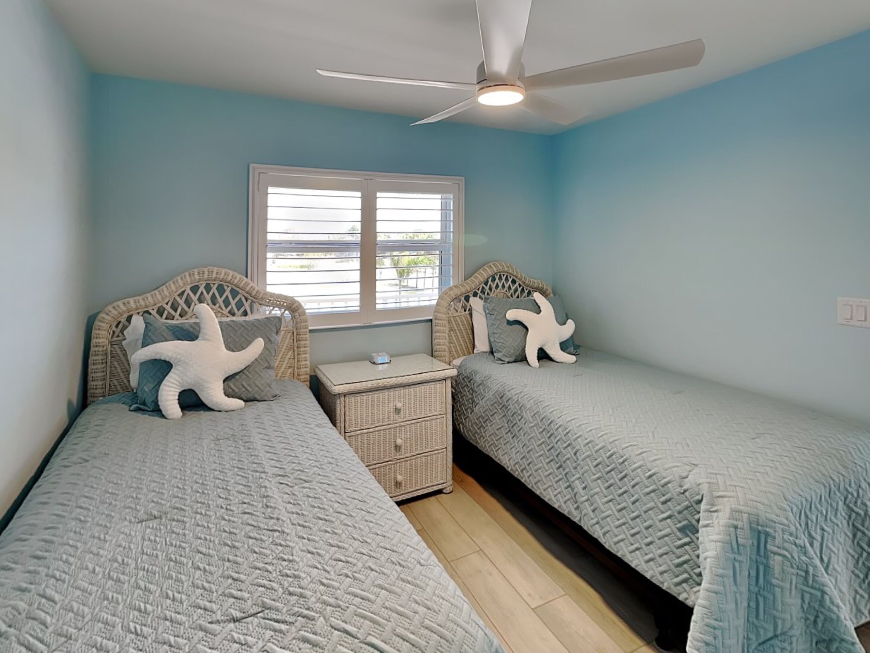 A bedroom with two beds, a ceiling fan, a window, and a nightstand.