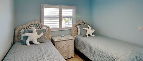 A bedroom with two beds, a ceiling fan, a window, and a nightstand.